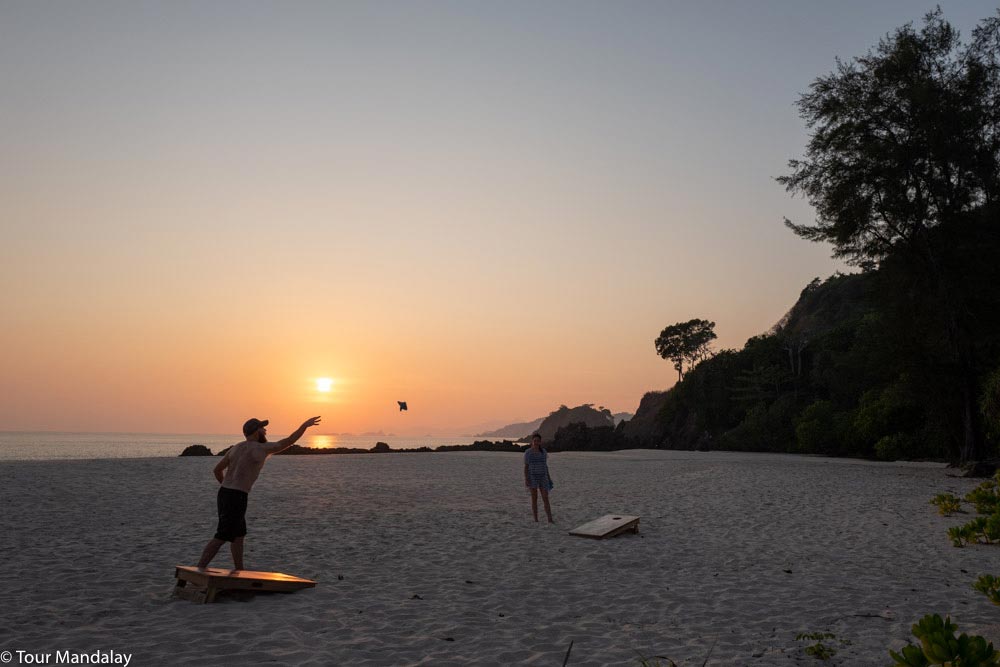 Man throws beanbag on beach at sunset